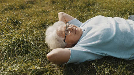 Cool grandma lying on the grass with hands under her head. Resting in nature. High quality photoの写真素材