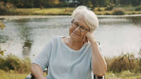 Pensive old woman in the wheelchair sitting near the river . High quality photo