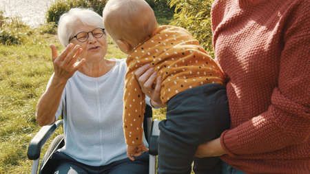 Happy family concept. Mother, grandmother in the wheelchair and baby having fun in nature. High quality photoの写真素材