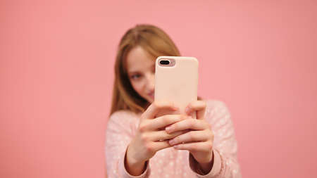 Young caucasian woman using smartphone and taking photos. Isolated on pink background. High quality...