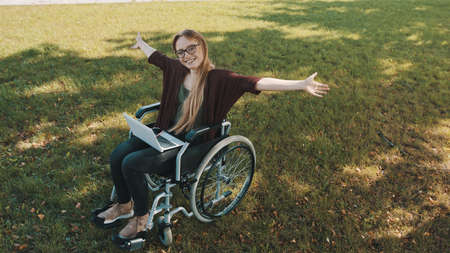 happy young disabled caucasian woman in the wheelchair resting in the nature with laptop and...