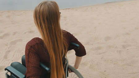 Young disabled woman on the sandy beach sitting in the wheelchair. High quality photo