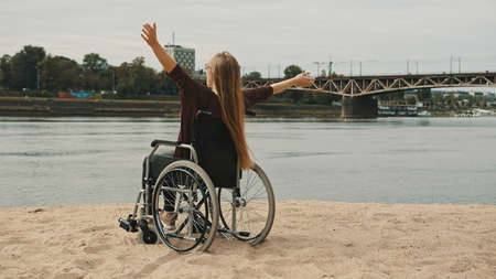 Happy young disabled woman in the wheelchair enjoying the vacation on the sandy river coast. High quality photoの写真素材