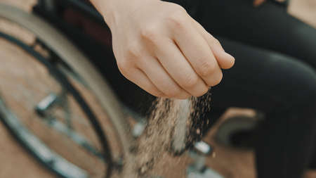 close up, hand of disabled person in the wheelchair playing with the sand on the beach. High quality photoの写真素材