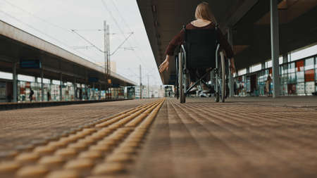 Low angle, young woman spinning the wheels of the wheelchair on the train station. High quality...