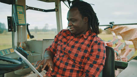 Young african farmer using tablet and smiling while sitting in the tractor cabin. High quality photo