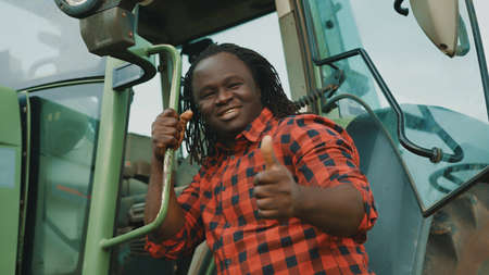 Young african man, farmer getting into tractor cabin with thumb up. High quality photo