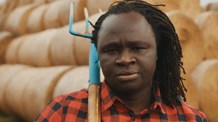 Portrait of young african farmer with pitchfork over his shoulder in front of haystack. High quality...