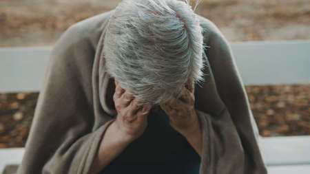 Poor sad homeless man crying on the bench covered with blanket. Social issues concept. High quality photoの写真素材