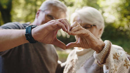 Lovely older retired couple making heart with their hands and looking at each other. Selective focus. High quality photoの写真素材