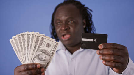 Confused African Man with Credit Card and Money - US Dollars - Cash or Card dillema. High quality 4k footageの写真素材