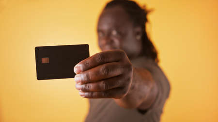 Happy african man in white showing credit card at camera over orange background.