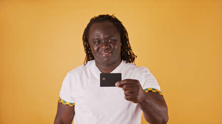 Happy african man in white showing credit card at camera over orange background.の写真素材