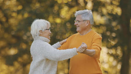 Happy old enjoying day in park. Senior man flirting with elderly woman. Dance in autumn day. High quality photoの写真素材