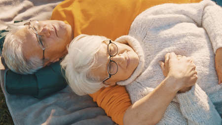 Romance at old age. Retired couple enjoying autumn day in park. Lying on the blanket and looking at each other. High quality photoの写真素材
