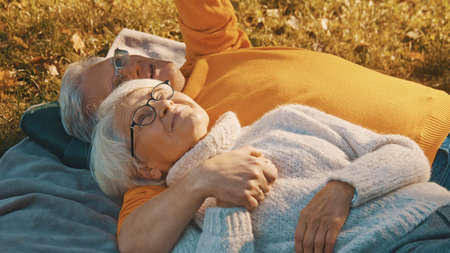 Romance at old age. Retired couple enjoying autumn day in park. Lying on the blanket and looking at each other. High quality photoの写真素材