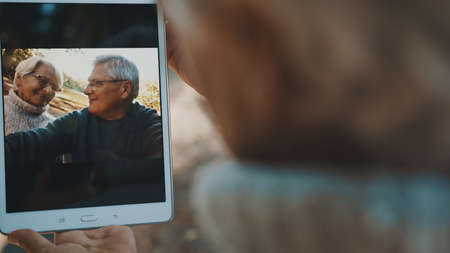 Mature couple in love taking selfie in forest on autumn day. Video call or browsing old photos. High quality photoの写真素材