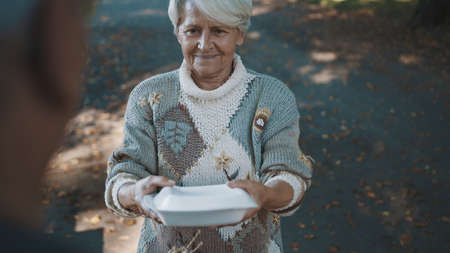 Old vulnerable homeless woman getting free charity meal. High quality photoの写真素材