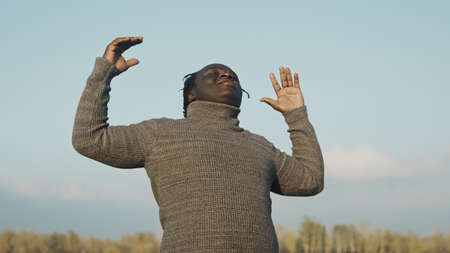 Young affrican man outstretching hands in the nature. Prayer or celebration. Medium shot. High...