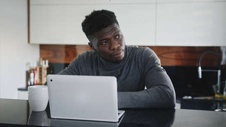 young african american black man working on laptop in his apartment stretching and looking through the window.の写真素材