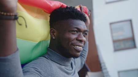 Black man holding rainbow flag and waving it behind his back from the balcony. Sexual identity...