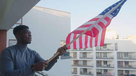 Young attractive black man waving American flag from the balcony. High quality photoの写真素材