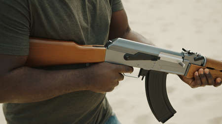 Violent man aiming with assault rifle while walking in desert area. High quality photo