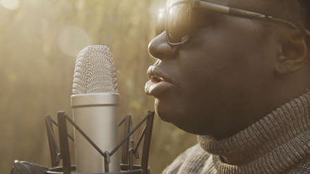Portrait shot of african american black man singing in the microphone in the woods. Natural light. High quality photoの写真素材