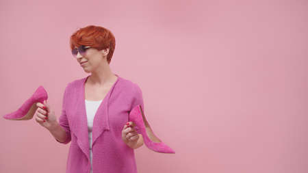 Mature woman with red short hair holding high heal shoes Isolated on purple background. High quality photoの写真素材