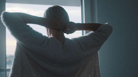 Young blonde woman stretching in front of the window. Back view. High quality photo