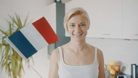 Young blond caucasian woman waving flag of france in her appartment. High quality photo