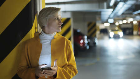Young scared blond woman using smartphone in the garage. High quality photo