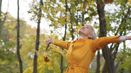 Happy caucasian woman trowing yellow autumn leaves in the park and spinning around. High quality...