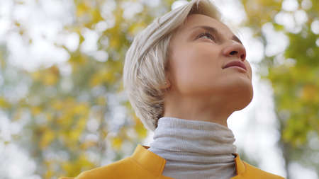 Portrait young blond fashionable woman in yellow coat in the park. High quality photo
