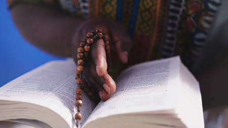 Unrecognizable African black man in traditional dress with rosary reading the Holy Bible . High...