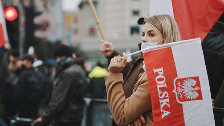 Warsaw, Poland 11.11.2020 - Independence day march on 102nd anniversary in Warsaw. Woman with face mask holding polish flag in crowd. High quality photoのeditorial素材