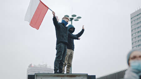 Warsaw, Poland 11.11.2020 - Independence day march on 102nd anniversary in Warsaw. Two young man waving polish flag. High quality photoのeditorial素材