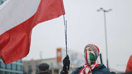 Warsaw, Poland 11.11.2020 - Independence day march on 102nd anniversary in Warsaw. Man with polish flag and facce mask in the crowd red flares . High quality photoのeditorial素材