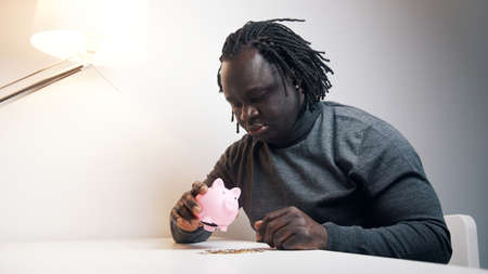 Depresed African american black man shaking empty piggy bank. . High quality photo