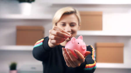 Savings concept. Happy caucasian blond woman pitting coins into the piggy bank. High quality photoの写真素材