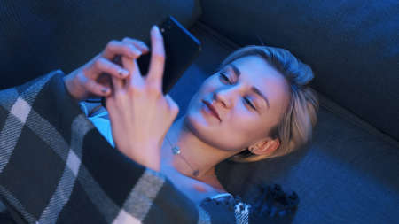 Excited young woman thinking about the sms or social media post while lying on the couch. High quality photoの写真素材