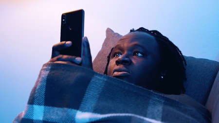 African american tired black man holding smartphone while lying on the couch . High quality photoの写真素材