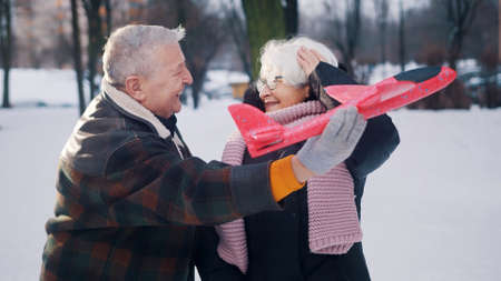 Happy elderly couple playing with airplane toy in the park in winter. . High quality photo
