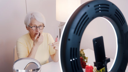 Elderly woman having a video call while applying make up and getting ready for valentines day date. High quality photoの写真素材