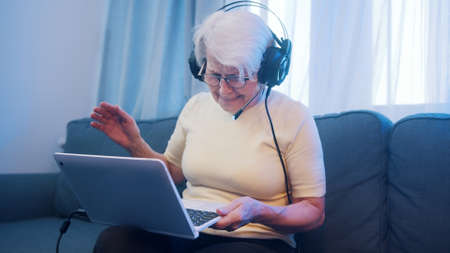 Elderly woman with headset having video call with family and waving to camera. Old people and technology. High quality photoの写真素材