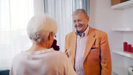 Valentines day and dating at old age. Elderly couple celebrating anniversary. Man giving red roses to his wife. High quality photoの写真素材