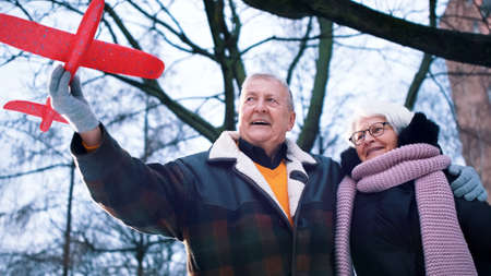 Happy elderly couple playing with airplane toy in the park in winter. High quality photoの写真素材