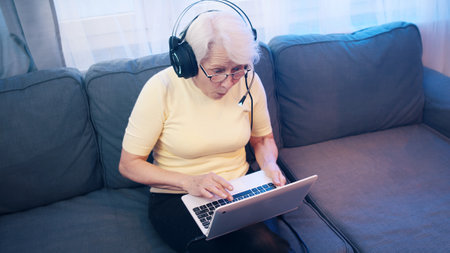 Elderly woman with headset having video call with family and waving to camera. Old people and technology. High quality photoの写真素材