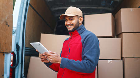Delivery man using tablet to preview orders. Standing in front of the van with parcels. High quality photoの写真素材