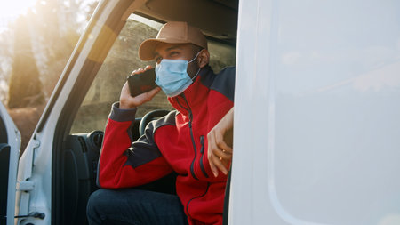 View through opened van doors on adult man siting inside and having phone call. Male worker wearing...